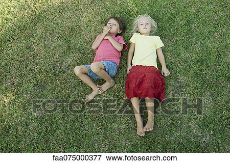 Children lying together on grass, looking up at camera View Large Photo Image Stock Photo - Children lying together on grass, looking up at camera. Fotosearch