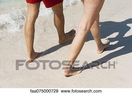 Stock Photo - Coupld walking on beach, low section. Fotosearch