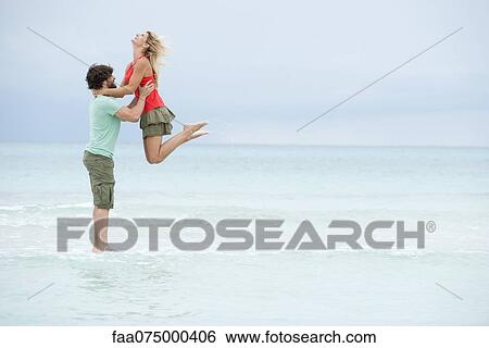 Stock Photograph - Couple at the beach, man lifting woman in air. Fotosearch