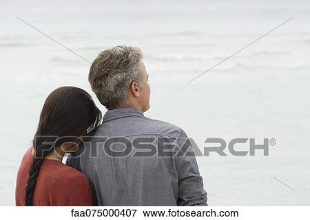 Stock Photo - Couple looking at sea together, rear view. Fotosearch