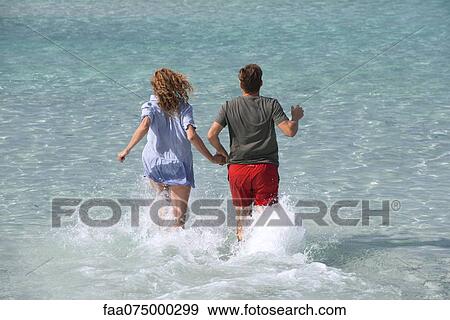 Couple running into water holding hands, rear view View Large Photo Image Stock Photo - Couple running into water holding hands, rear view. Fotosearch