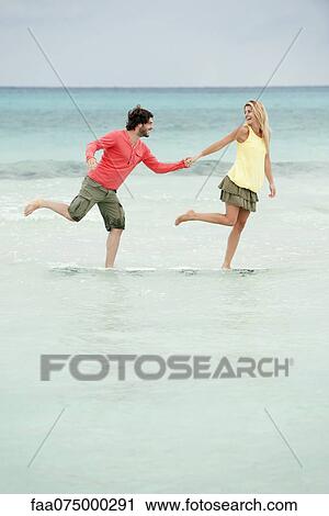 Couple standing on one leg in water at the beach, holding hands View Large Photo Image Stock Image - Couple standing on one leg in water at the beach, holding hands. Fotosearch