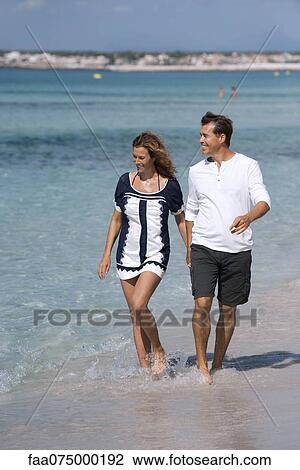 Couple walking on beach holding hands, ankles deep in water View Large Photo Image Stock Image - Couple walking on beach holding hands, ankles deep in water. Fotosearch