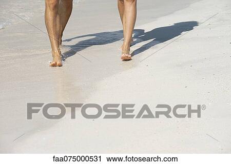 Stock Image - Couple walking on beach, low section. Fotosearch