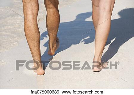 Stock Photo - Couple walking on beach, low section. Fotosearch