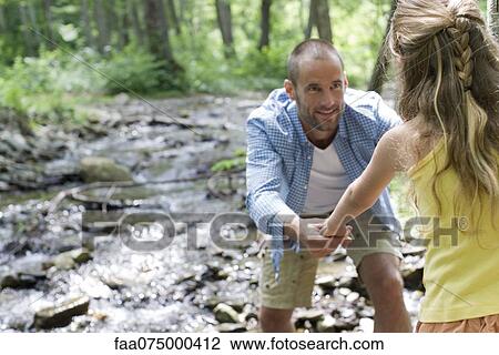 Stock Image - Father helping daughter crossing stream. Fotosearch