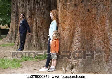 Father leaning against tree trunk in background, wife and daughter separate in foreground View Large Photo Image Stock Photograph - Father leaning against tree trunk in background, wife and daughter separate in foreground. Fotosearch