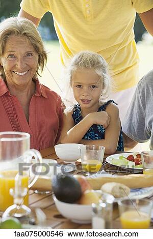 Stock Photograph - Girl and grandmother at breakfast table outdoors, cropped. Fotosearch