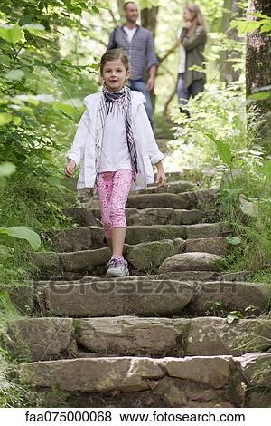 Stock Photo - Girl walking down stone steps in woods, parents in background. Fotosearch