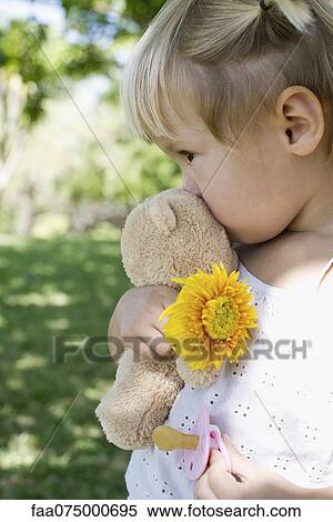 Stock Photography - Little girl holding teddy bear, flower and pacifier. Fotosearch