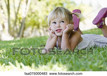 Stock Image - Little girl lying on grass, looking up. Fotosearch