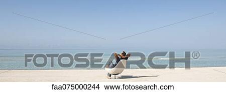 Man relaxing in chair on beach, rear view View Large Photo Image Picture - Man relaxing in chair on beach, rear view. Fotosearch