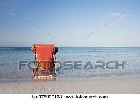 Stock Photo - Man sitting in deckchair looking at ocean, rear view. Fotosearch