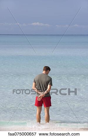 Man standing ankle deep in water contemplating ocean, rear view View Large Photo Image Stock Photo - Man standing ankle deep in water contemplating ocean, rear view. Fotosearch