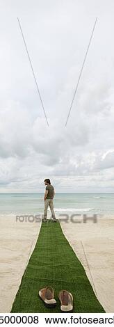 Man standing at end of carpet on beach, sandals on foreground View Large Photo Image Stock Photo - Man standing at end of carpet on beach, sandals on foreground. Fotosearch