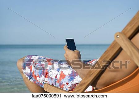 Man using cell phone while sitting on beach, cropped View Large Photo Image Stock Image - Man using cell phone while sitting on beach, cropped. Fotosearch
