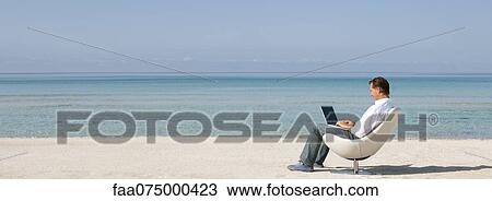 Stock Image - Man using laptop computer at the beach. Fotosearch