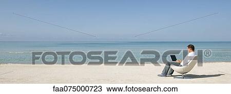Stock Image - Man using laptop computer at the beach. Fotosearch