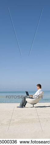 Stock Photograph - Man using laptop computer at the beach. Fotosearch