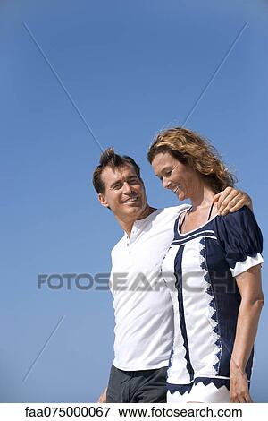 Stock Photo - Smiling couple outdoors, low angle view, portrait. Fotosearch