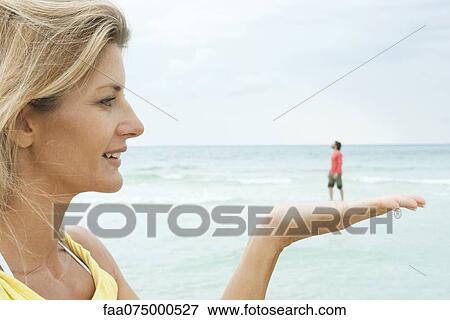 Woman appearing to hold tiny man in her hand at the beach View Large Photo Image Stock Photo - Woman appearing to hold tiny man in her hand at the beach. Fotosearch