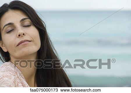 Stock Image - Woman at the beach, eyes closed, portrait. Fotosearch