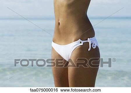 Stock Photograph - Woman in bikini at the beach, mid section. Fotosearch