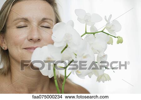 Picture - Woman smelling orchids, eyes closed. Fotosearch