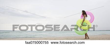 Woman standing on beach, holding inflatable rings, side view View Large Photo Image Stock Photography - Woman standing on beach, holding inflatable rings, side view. Fotosearch