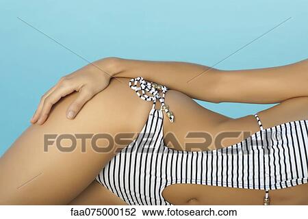 Stock Image - Woman sunbathing beside pool, mid section. Fotosearch