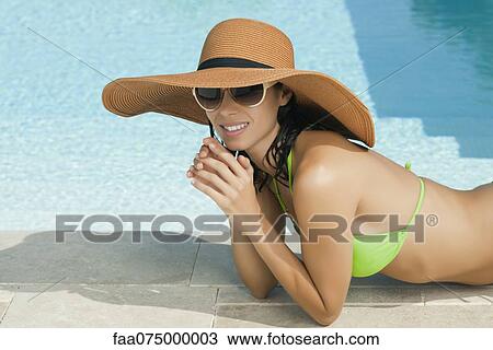 Stock Image - Woman sunbathing beside pool, portrait. Fotosearch