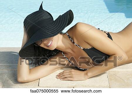 Woman sunbathing beside pool, wearing sun hat View Large Photo Image Stock Photography - Woman sunbathing beside pool, wearing sun hat. Fotosearch