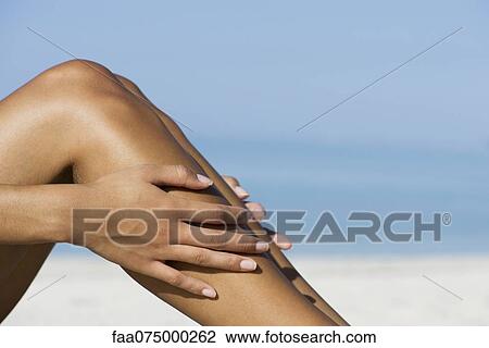 Stock Image - Woman touching bare legs at the beach, cropped. Fotosearch
