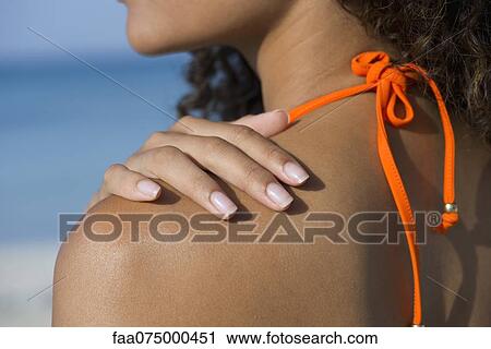 Stock Image - Woman touching bare shoulder at the beach, cropped. Fotosearch