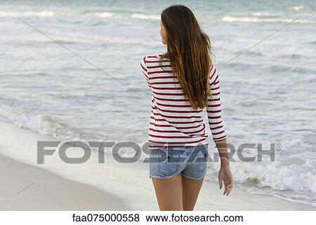 Stock Photo - Woman walking on beach, rear view. Fotosearch