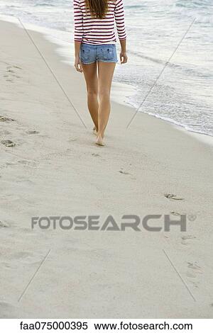 Stock Photography - Woman walking on beach, rear view, cropped. Fotosearch