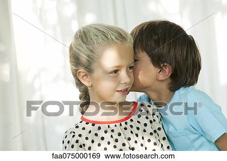 Stock Photo - Young boy whispering secret in girl's ear. Fotosearch