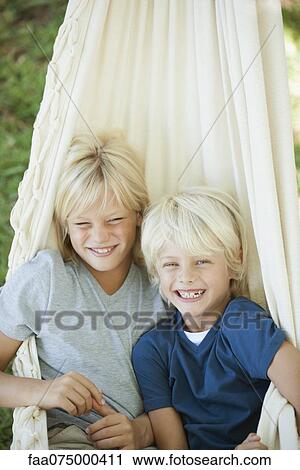 Stock Image - Young brothers sitting together in hammock, portrait. Fotosearch