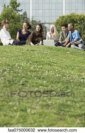 Stock Image - Young friends spending time outdoors on grass, low angle view. Fotosearch