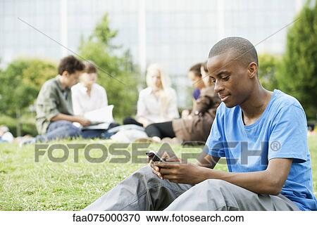 Young man text messaging with cell phone, people in background View Large Photo Image Stock Image - Young man text messaging with cell phone, people in background. Fotosearch