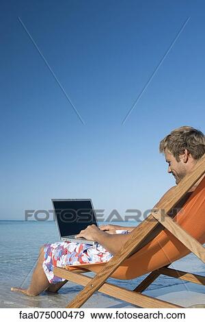 Young man using laptop on beach View Large Photo Image Stock Photo - Young man using laptop on beach. Fotosearch