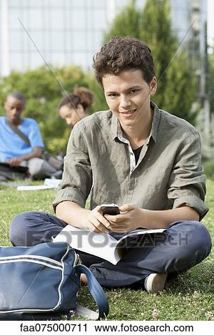 Stock Image - Young man with cell phone, friends in background, portrait. Fotosearch