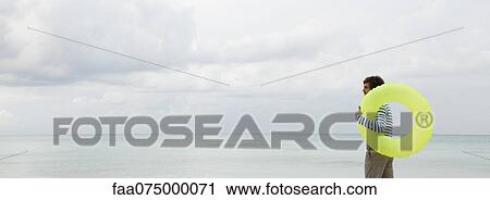 Young man with inflatable ring, looking at ocean View Large Photo Image Stock Image - Young man with inflatable ring, looking at ocean. Fotosearch