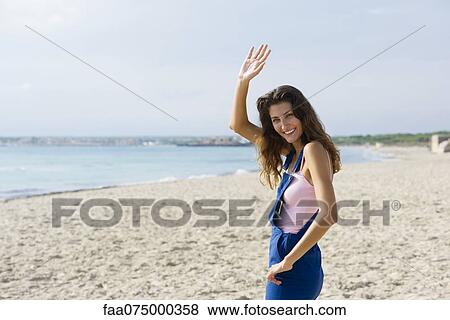 Young woman at the beach, smiling and waving at camera View Large Photo Image Stock Photo - Young woman at the beach, smiling and waving at camera. Fotosearch