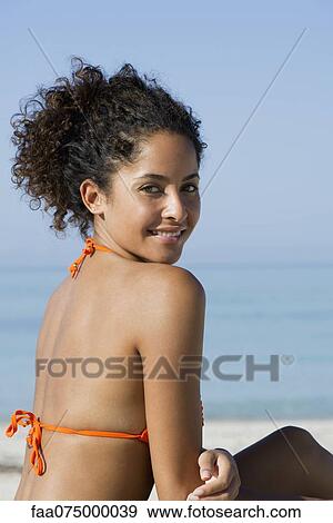 Young woman at the beach, smiling over shoulder, portrait View Large Photo Image Stock Photo - Young woman at the beach, smiling over shoulder, portrait. Fotosearch