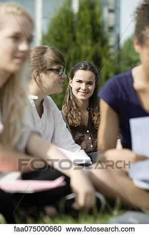 Stock Image - Young woman hanging out with friends outdoors, focus on woman in background. Fotosearch