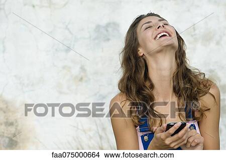 Young woman holding cell phone, laughing View Large Photo Image Picture - Young woman holding cell phone, laughing. Fotosearch