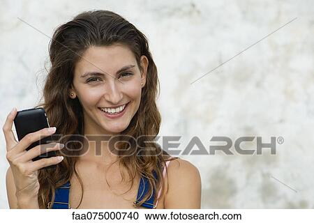 Young woman holding cell phone, smiling, portrait View Large Photo Image Stock Image - Young woman holding cell phone, smiling, portrait. Fotosearch