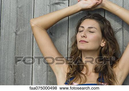 Stock Photo - Young woman leaning against wall with eyes closed, portraite. Fotosearch