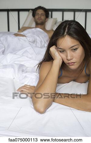 Young woman lying on bed looking down, boyfriend in background View Large Photo Image Stock Image - Young woman lying on bed looking down, boyfriend in background. Fotosearch